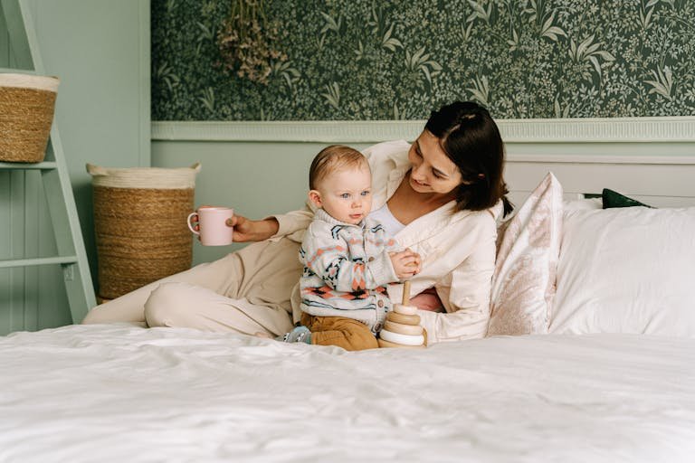 A mother shares a warm moment with her child on a cozy bed with wooden toys.