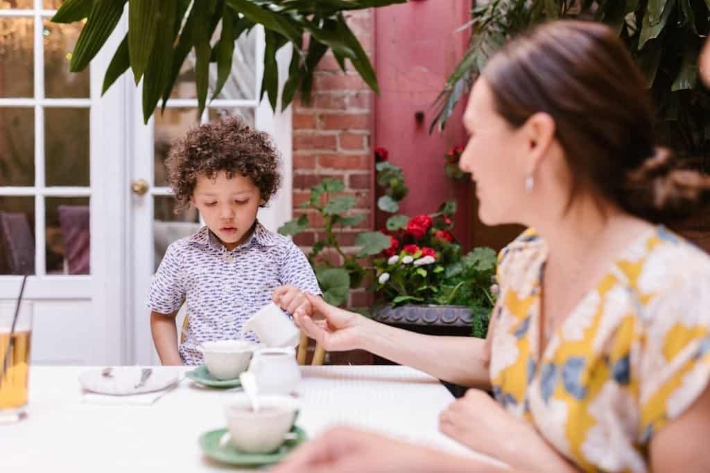 Heartwarming scene of a mother and son enjoying tea time together outdoors with lush greenery.