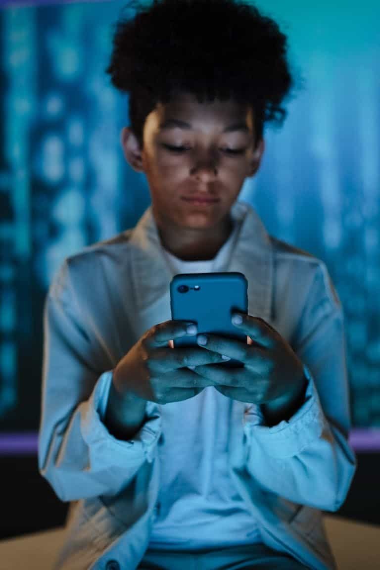 A teenager engrossed in using a smartphone with a blurred background for a modern conceptual shot.